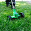Osoba používa zelený vyžínač s kolieskami na kosenie trávy.