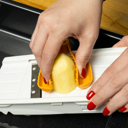 Ruka krája zemiak pomocou strúhadla, ktorý je držiavaný žltým chráničom prstov.